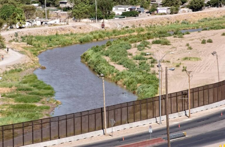 Beyond a bridge that crosses it, a river turns to the right through an arid landscape. Beyond a bridge that crosses it, a river turns to the right through an arid landscape.